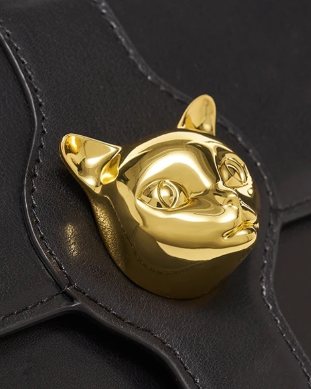 Close-up of gold cat emblem clasp on black shoulder bag by Bafelli with fine leather stitching