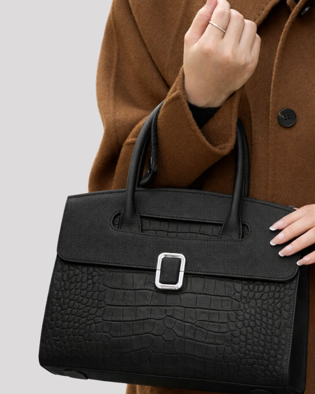 Close-up detail of silver buckle on black croc-embossed leather handbag