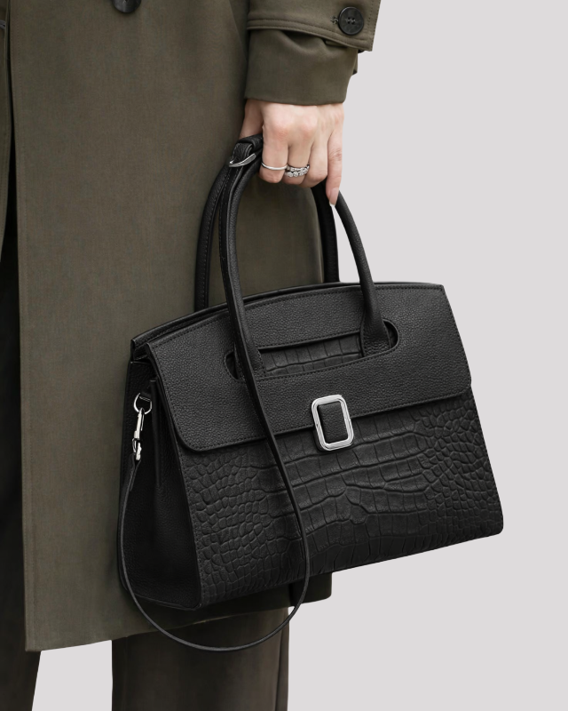 Black croc-embossed leather handbag carried by model showing size, top handles and shoulder strap
