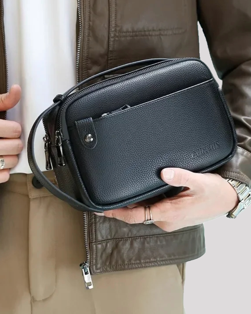 Black leather clutch bag held in front with hand resting on zipper pocket – lifestyle view