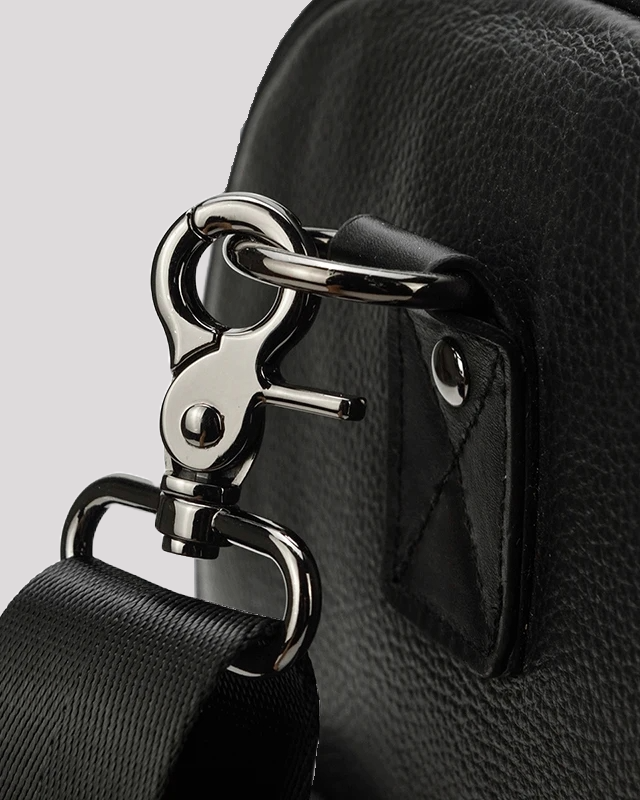 Close-up of silver clasp and D-ring detail on black leather travel duffel bag