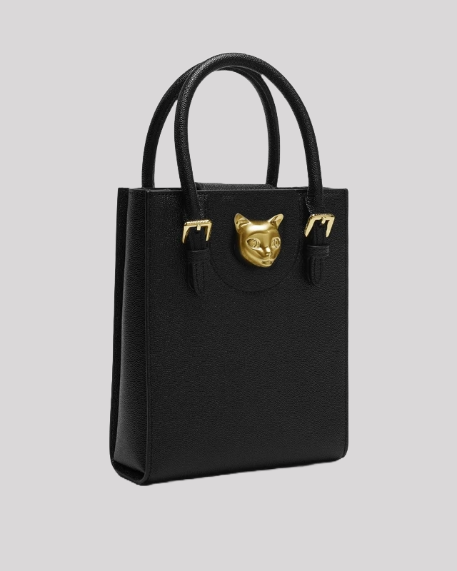 Side angle view of black tote bag by Bafelli with structured silhouette, dual handles, and gold cat head accent