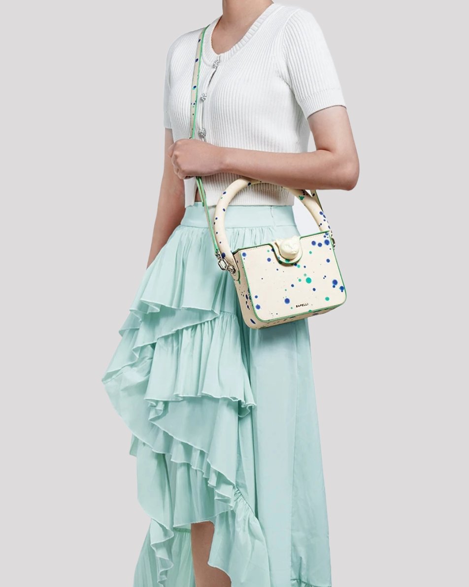Woman holding Blue Green Splatter Cat Bag by Bafelli by top handle – styled with mint skirt outfit