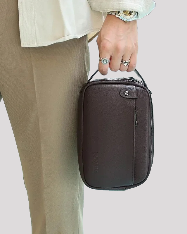 Man carrying brown leather men’s handbag by top handle – lifestyle view
