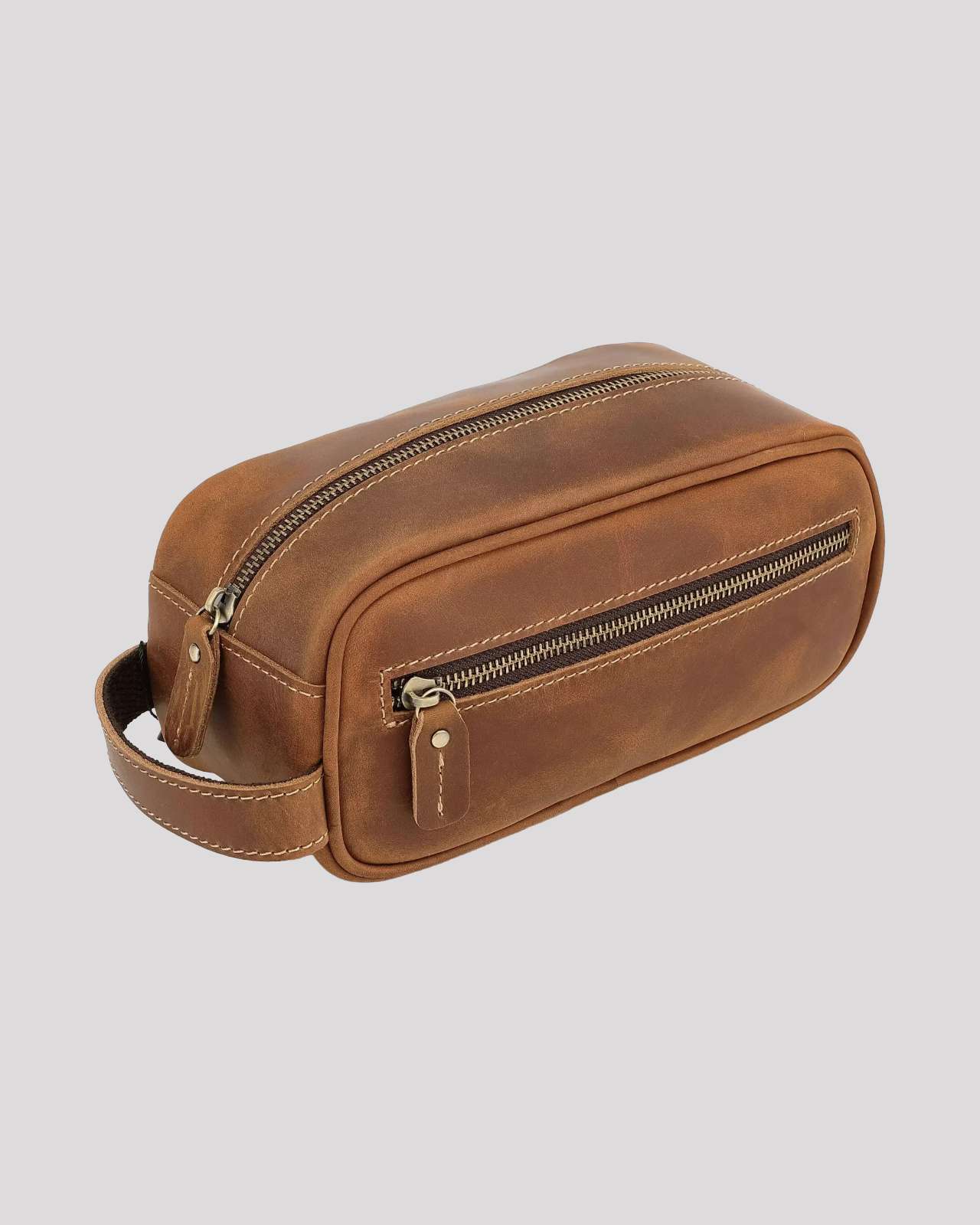 Side angle of brown leather toiletry bag with top zipper, front pocket zipper, and carry handle