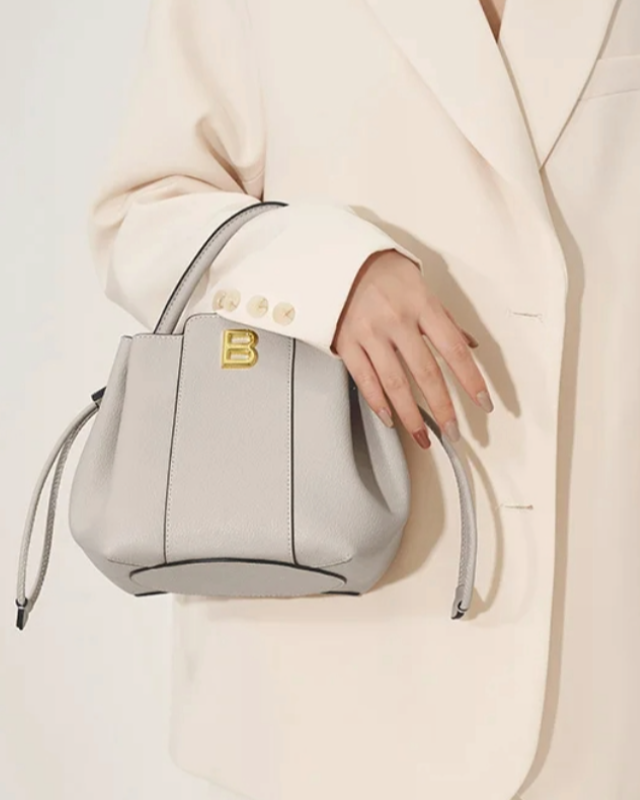 Model holding gray textured leather bucket bag by Bafelli with gold B logo and top handle design