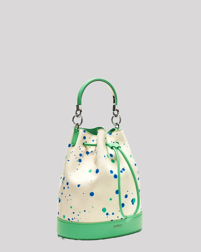Side angle of structured white leather bucket bag by Bafelli with blue and green paint splatter, green leather accents, and detachable handle