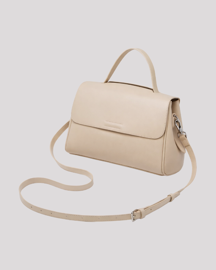 Front angled view of minimal beige leather top handle bag with adjustable shoulder strap