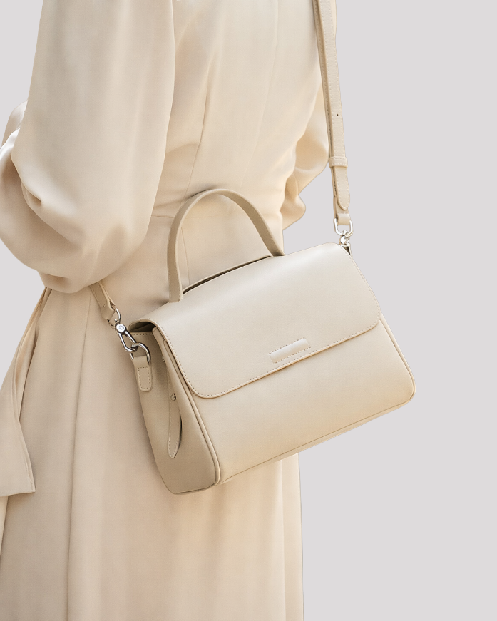 Minimal beige leather top handle bag worn crossbody by model, showing strap length and side profile