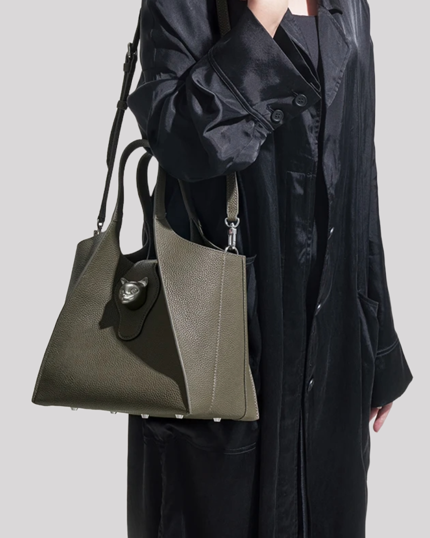 Model wearing olive green leather tote bag by Bafelli with structured shape and silver cat clasp on shoulder
