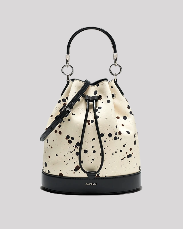 Front view of cream bucket bag by Bafelli with black paint splatter, black leather trim, silver hardware and structured base
