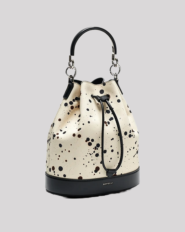 Side view of cream bucket bag by Bafelli with black paint splatter, black leather trim and detachable crossbody strap
