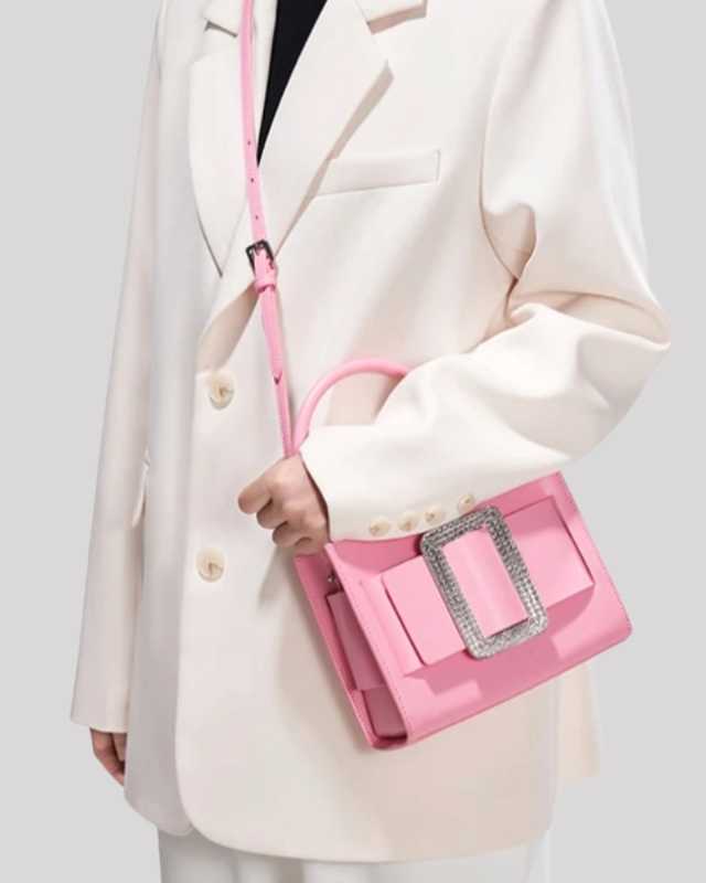 Pink top-handle bag by Bafelli worn over the shoulder with rhinestone buckle detail