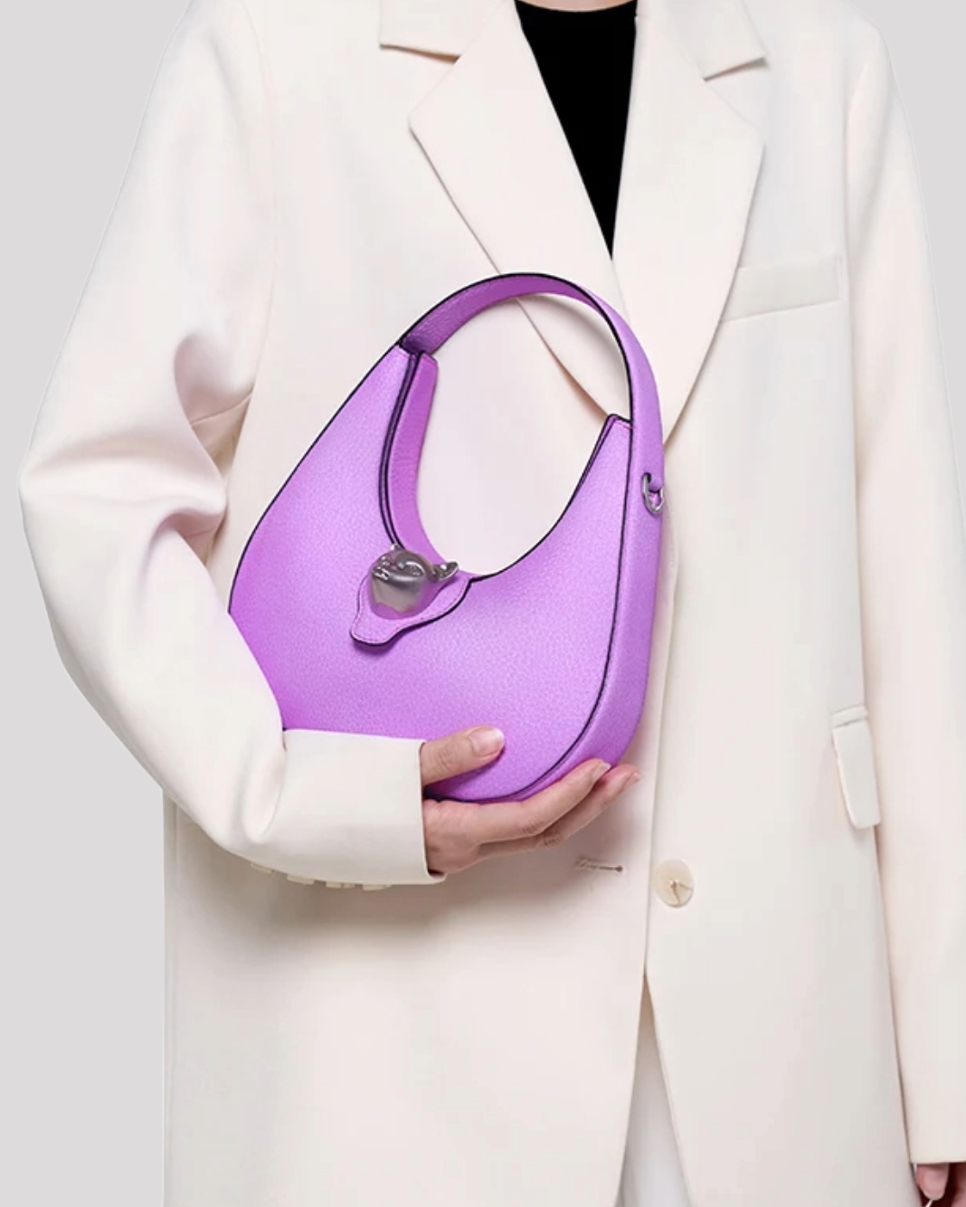 Woman in cream blazer holding purple leather hobo bag by Bafelli with cat clasp – lifestyle view