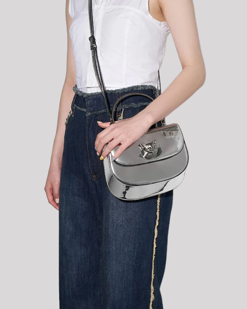 Silver metallic handbag by Bafelli with cat emblem worn crossbody by model