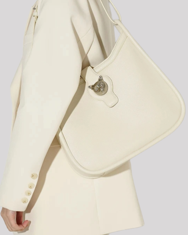 White leather shoulder bag with cat head clasp shown on model’s side in cream suit