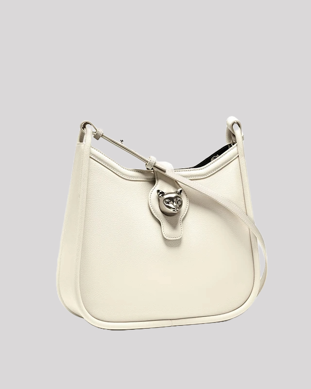 Side angle view of white leather shoulder bag by Bafelli with cat head clasp and long strap