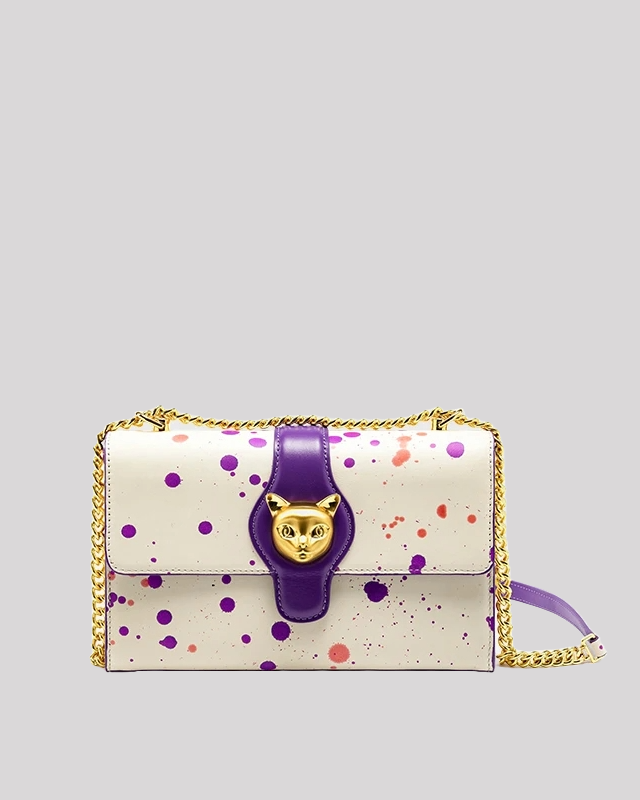 Front view of white shoulder bag with purple paint splatter design, purple strap, gold-tone cat head clasp, and chain strap by Bafelli