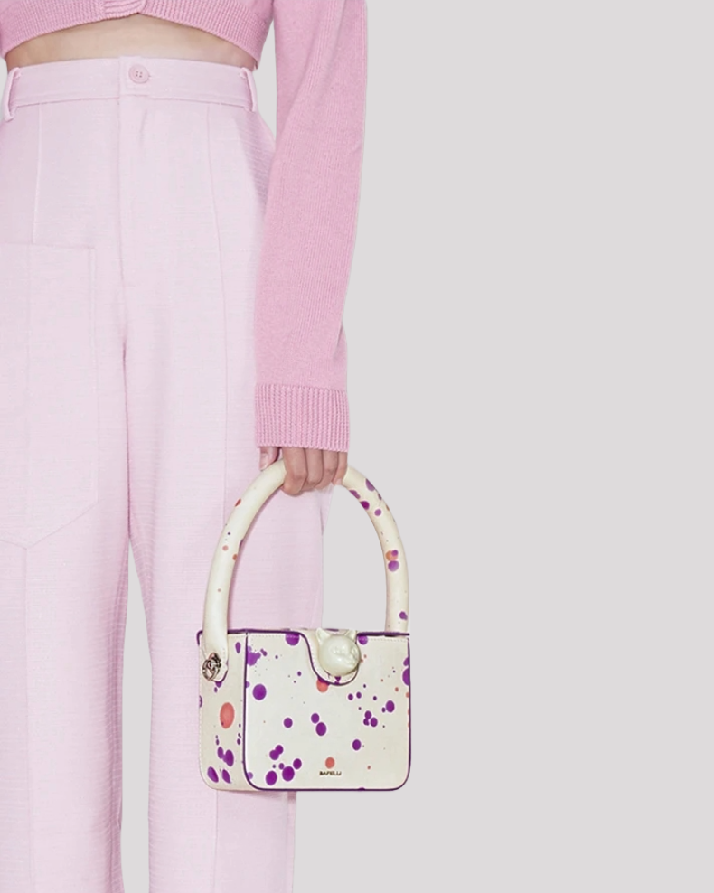 Close-up of woman carrying white mini bag by Bafelli with purple and pink splatter design