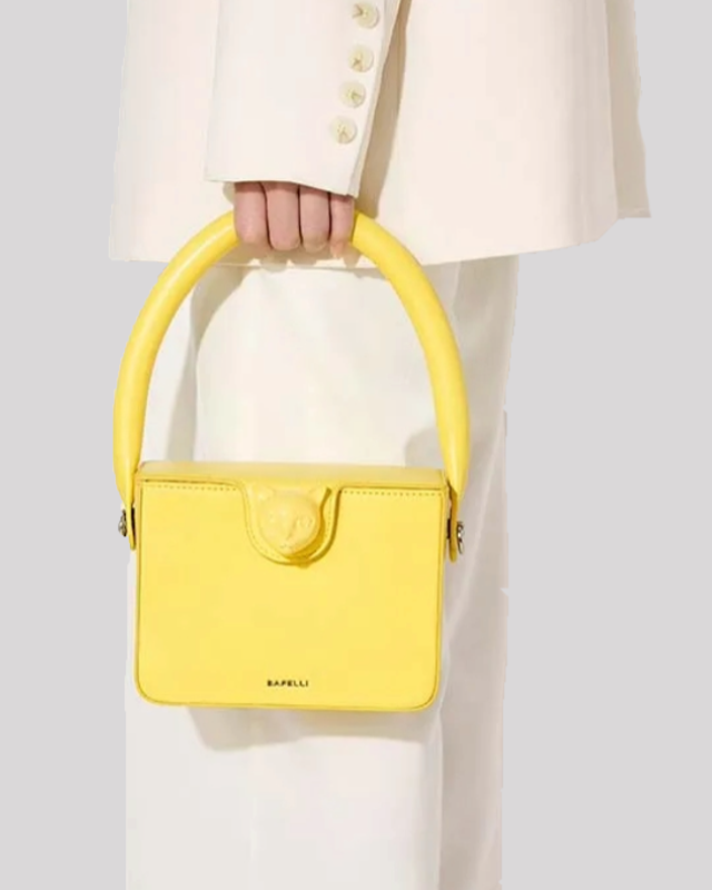 Model holding yellow Bafelli cat-handle bag by the rounded top handle