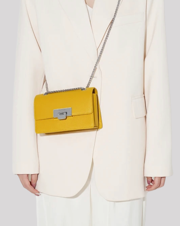 Yellow mini crossbody bag by Bafelli worn on shoulder with silver chain strap and metallic clasp closure