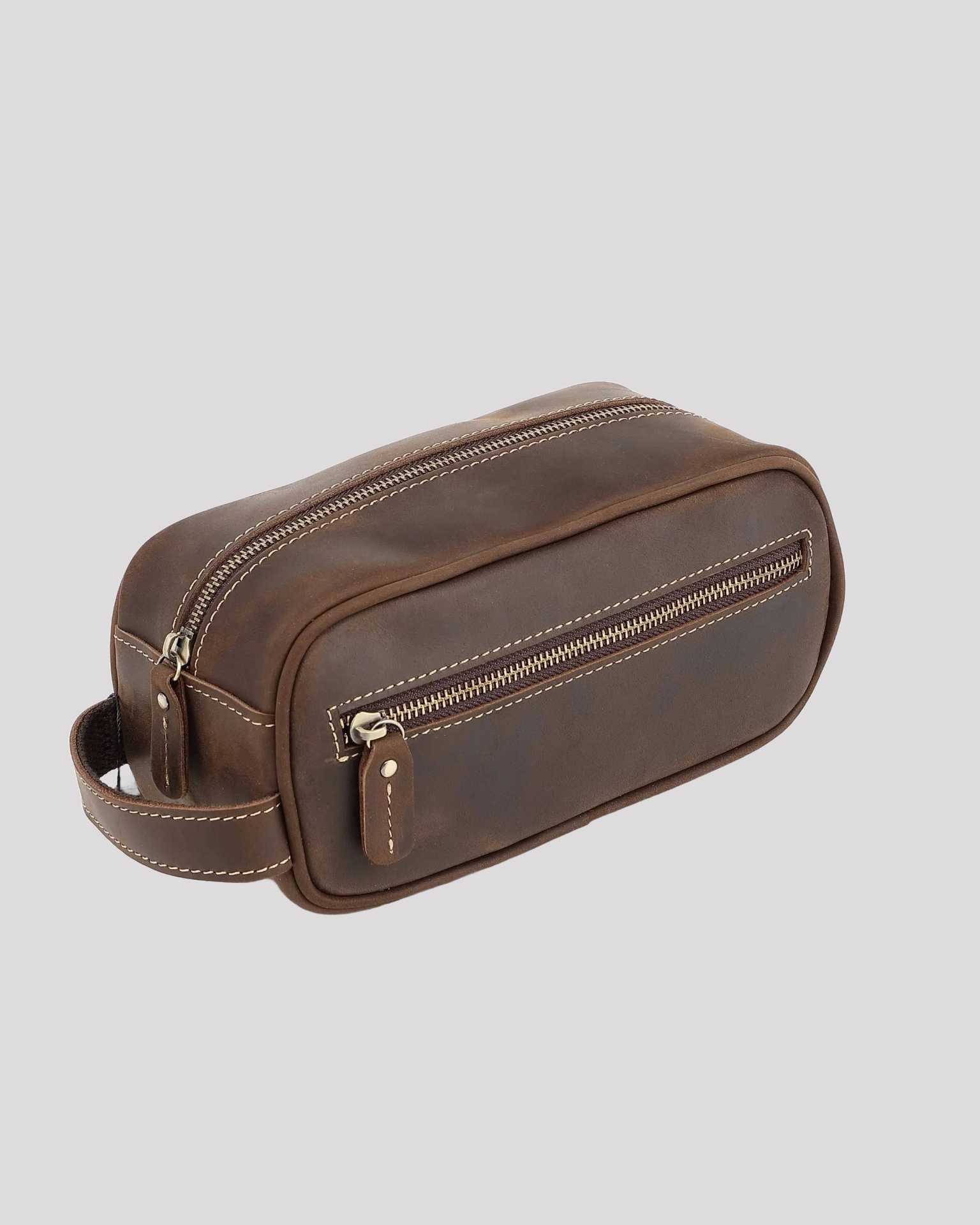 Angle view of dark brown leather toiletry bag with side handle and front zipper pocket