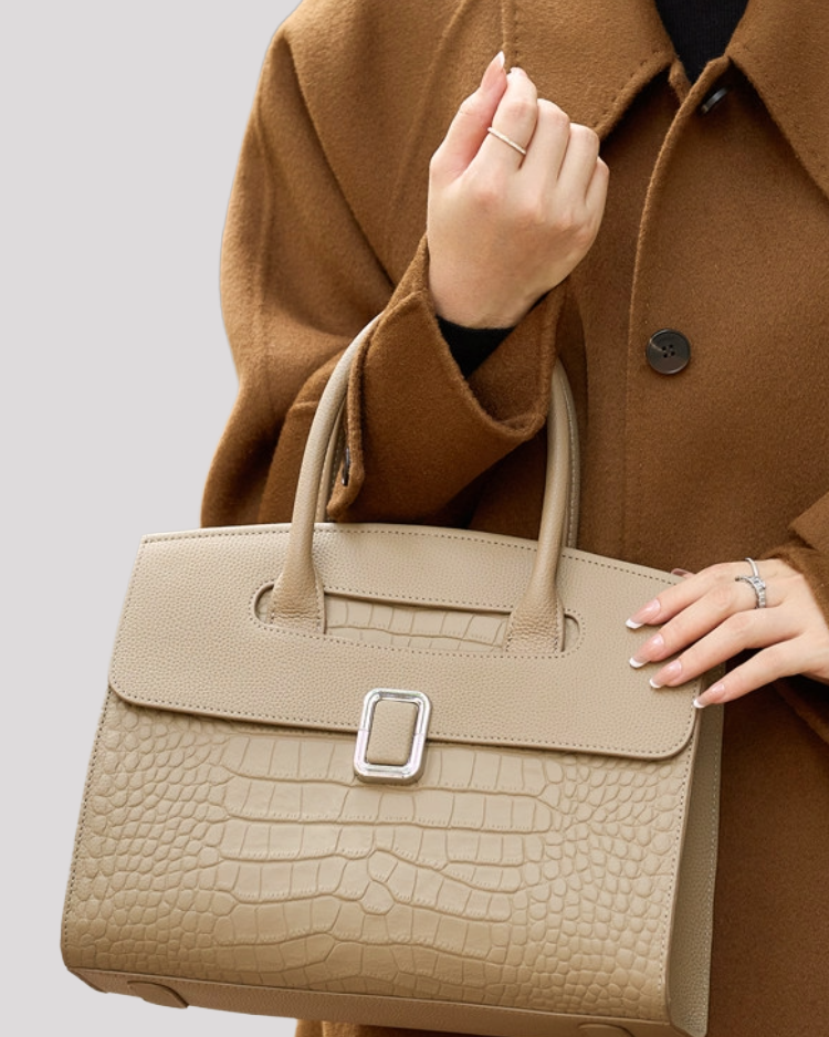 Close-up detail of silver buckle on beige croc-embossed leather handbag