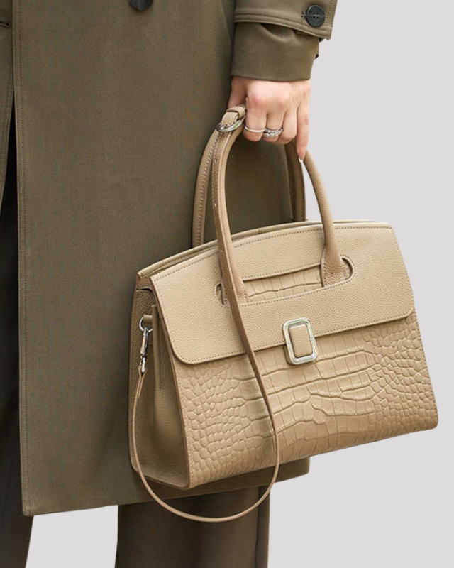 Beige croc-embossed leather handbag carried by model showing size, top handles and shoulder strap