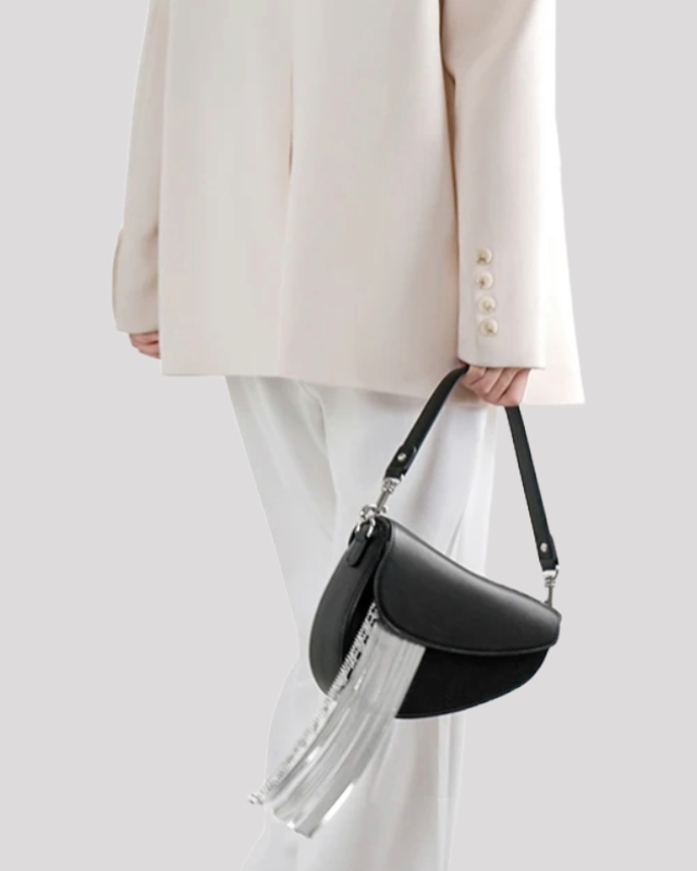 Model holding black asymmetric shoulder bag by Bafelli with silver fringe chain detail, styled with a white outfit