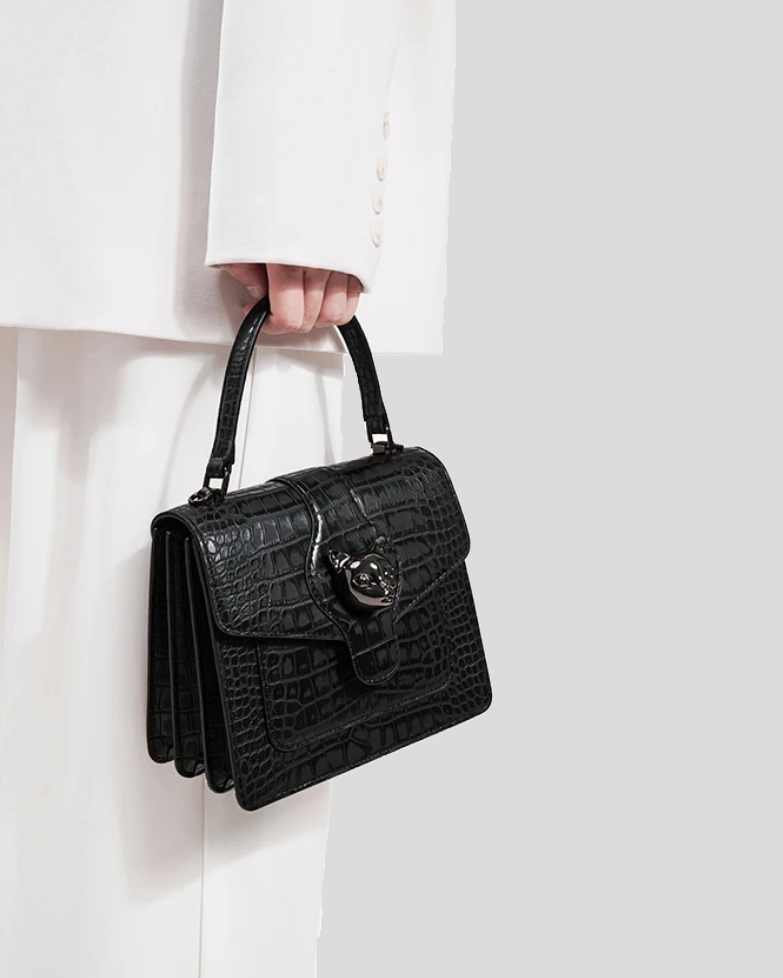 Woman holding black croc-embossed leather handbag by Bafelli by top handle – side lifestyle view