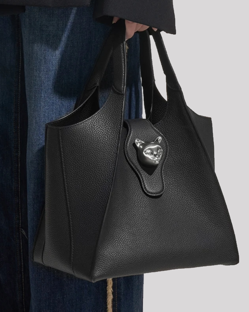 Black leather tote bag by Bafelli with silver cat emblem shown handheld for size reference