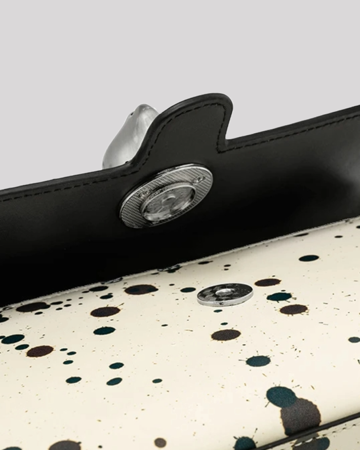 Close-up of silver cat clasp and snap closure on black splatter paint shoulder bag by Bafelli
