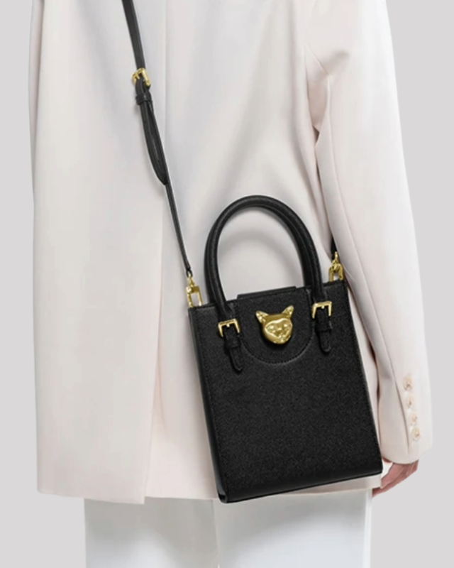 Black tote bag by Bafelli styled as a crossbody with long strap, worn by model in light outfit