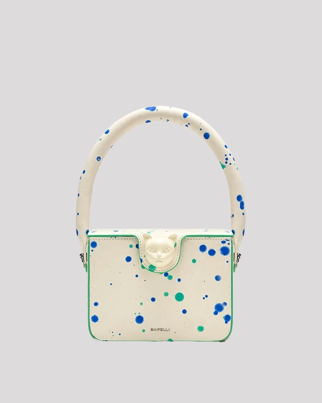 Front view of white Splatter Cat Bag by Bafelli with blue and green paint splatter design and cat head clasp