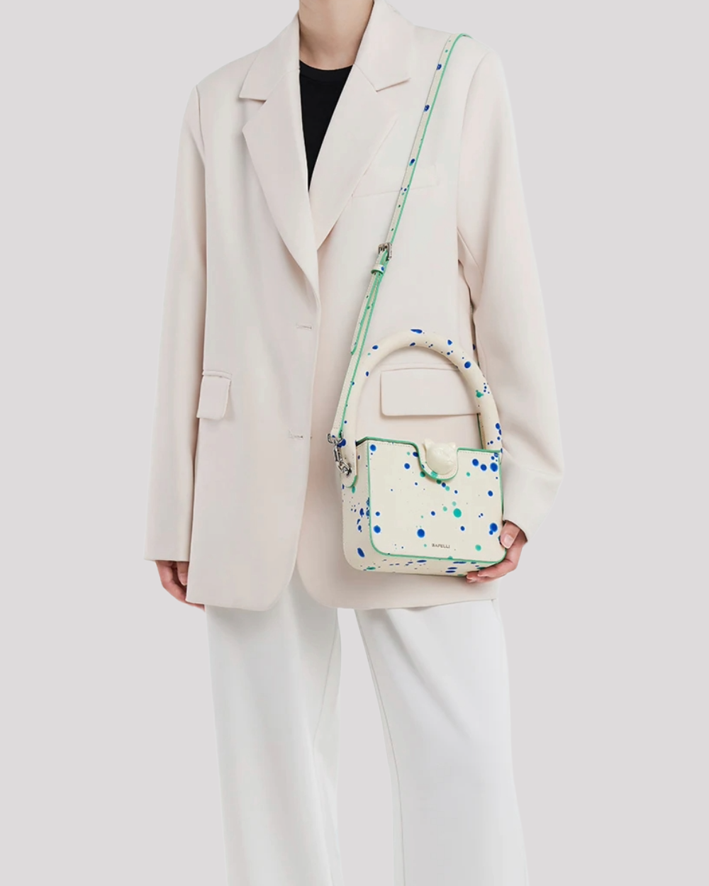 Woman wearing white blazer carrying Blue Green Splatter Cat Bag by Bafelli with shoulder strap – lifestyle view