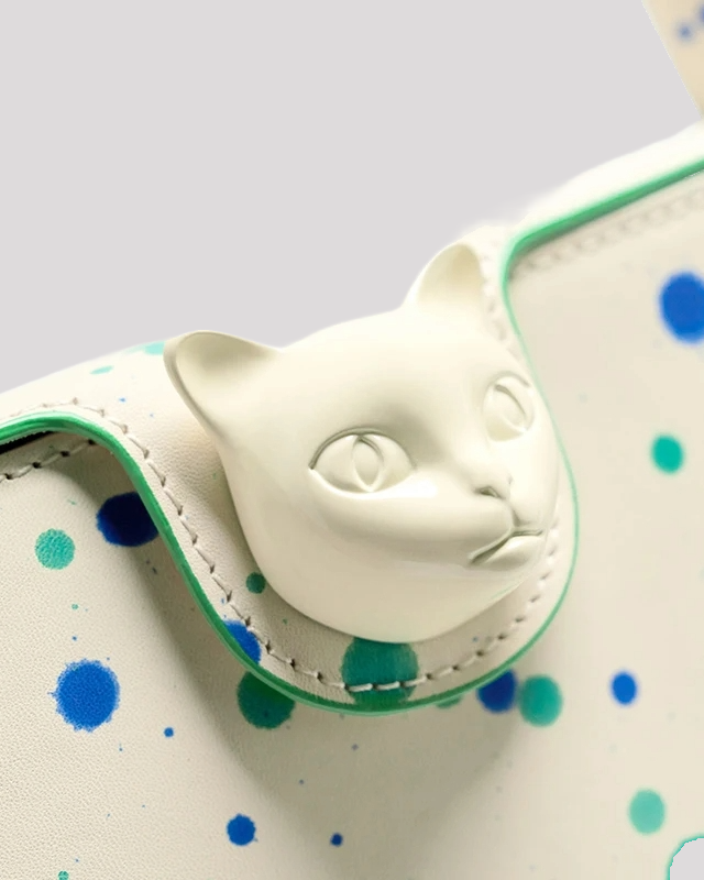 Macro close-up of white cat head clasp by Bafelli with surrounding blue and green paint splatters