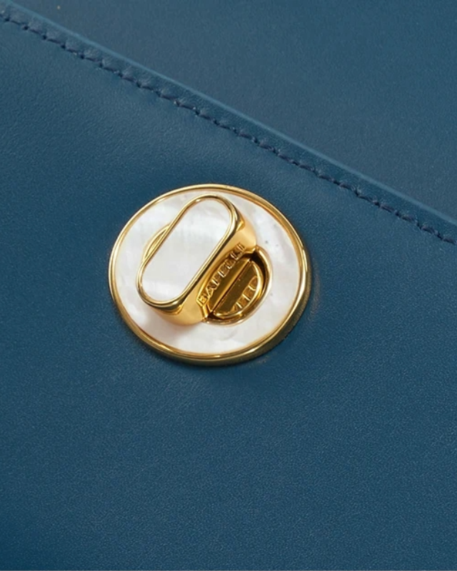 Close-up of gold and pearl turn-lock closure on blue structured top handle bag by Bafelli with engraved branding