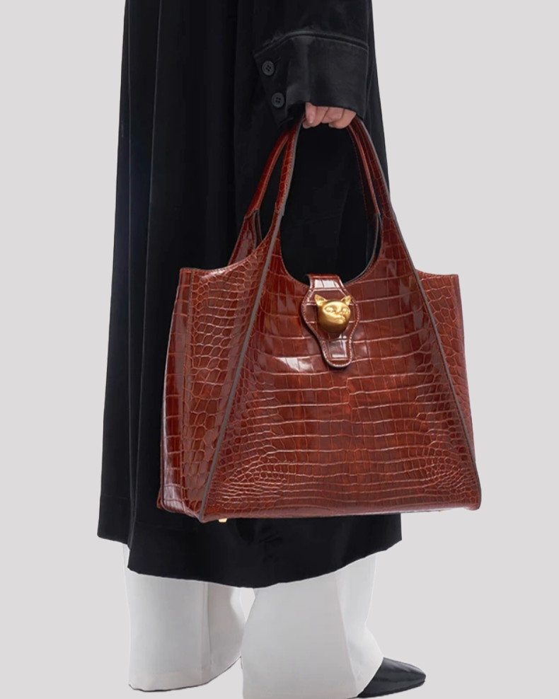 Brown croc-embossed tote bag by Bafelli with gold cat clasp styled with model in black coat and white pants