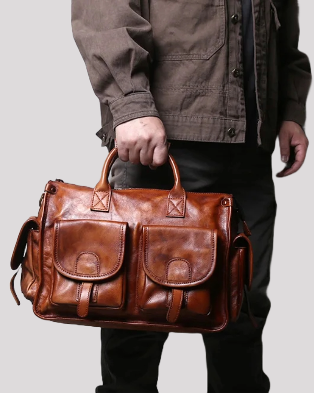 Brown vintage leather messenger bag carried by hand, showing scale and front pockets