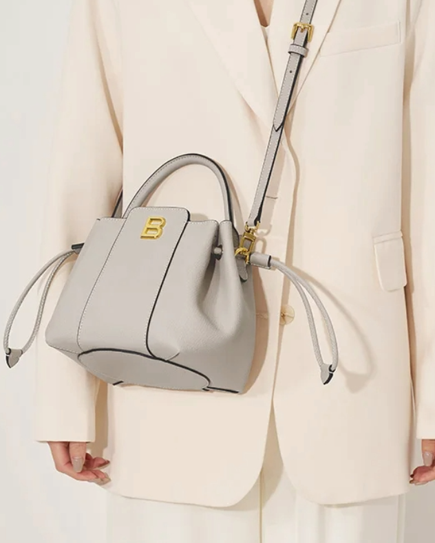 Model wearing gray textured leather bucket bag by Bafelli crossbody with adjustable strap and drawstring details