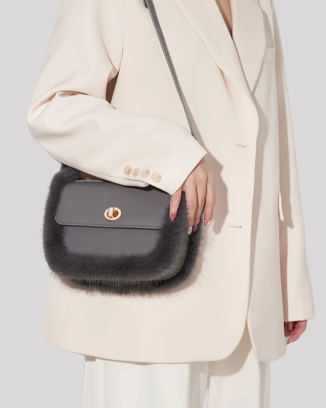 Grey fur-trim crossbody bag by Bafelli held by model wearing cream blazer