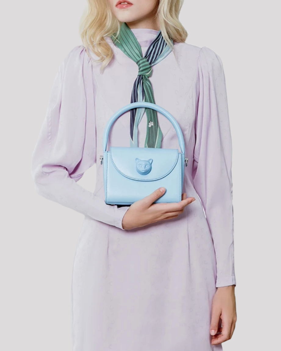 Woman holding light blue cat-embellished handbag by Bafelli while wearing a lilac dress and green scarf