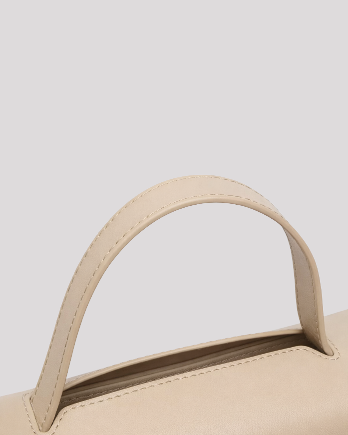Close-up detail of stitched top handle on minimal beige leather handbag