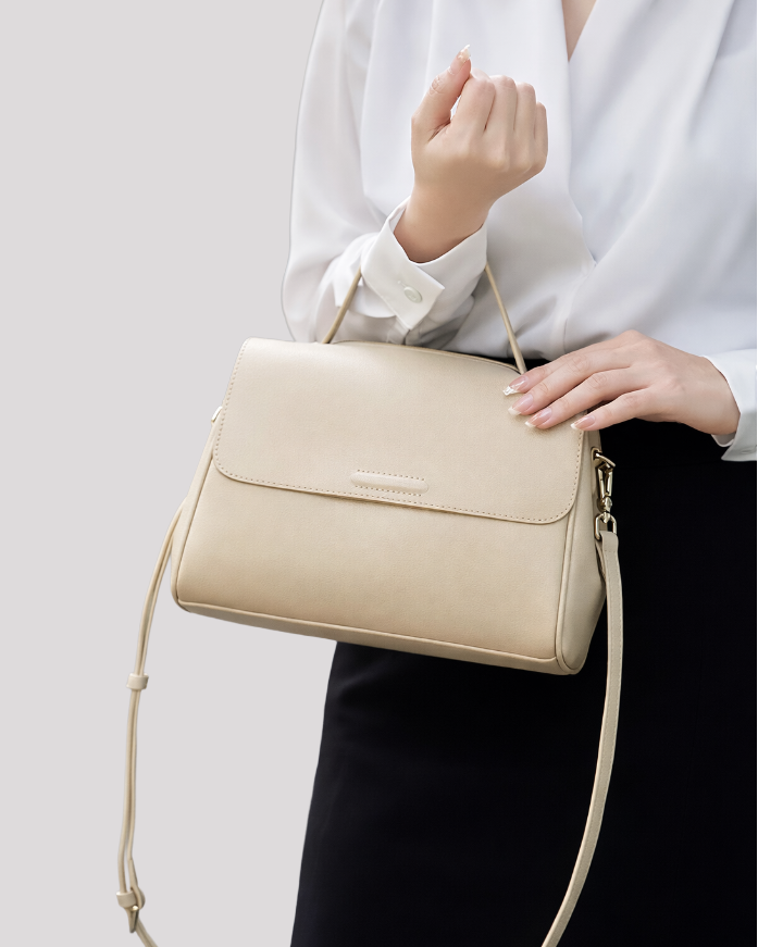 Minimal beige leather top handle bag carried by model from the front, highlighting elegant proportions