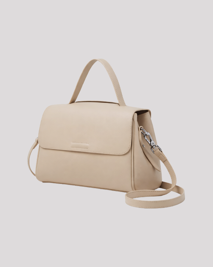 Side angle view of minimal beige leather top handle bag showing structured silhouette and silver hardware