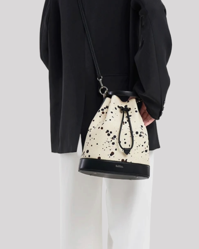 Model wearing cream bucket bag by Bafelli with black paint splatter as crossbody, styled with black blazer and white trousers