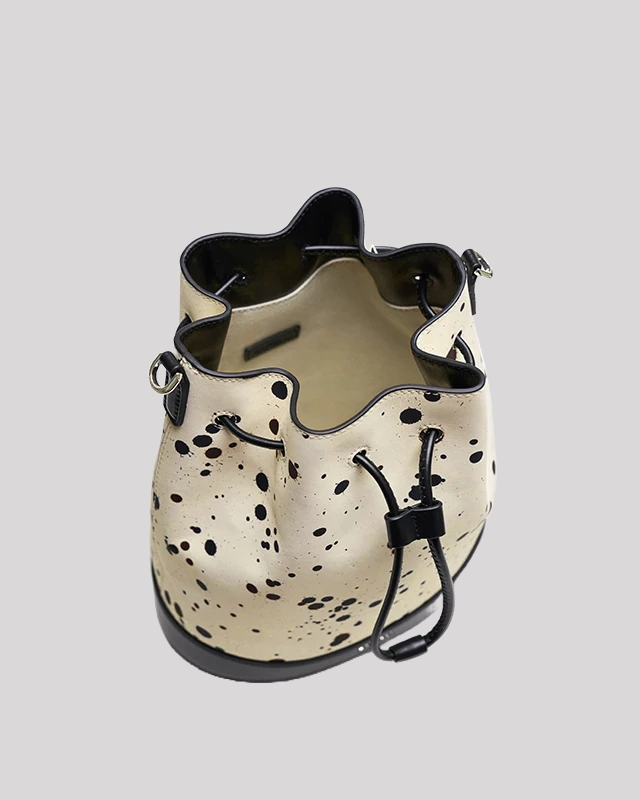 Inside view of cream bucket bag by Bafelli with black paint splatter, showing open compartment, black leather trim and drawstring fastening