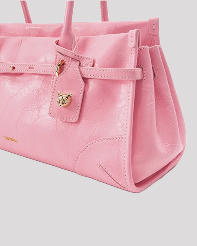 Close-up of pink leather shoulder bag by Bafelli showing gold cat charm and textured leather