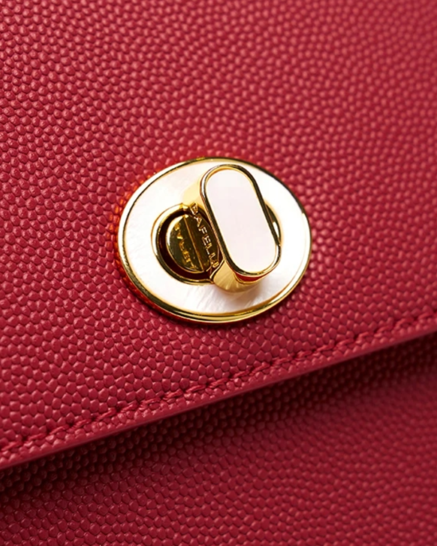 Close-up of gold turn-lock closure on red crossbody bag by Bafelli with fine textured leather details