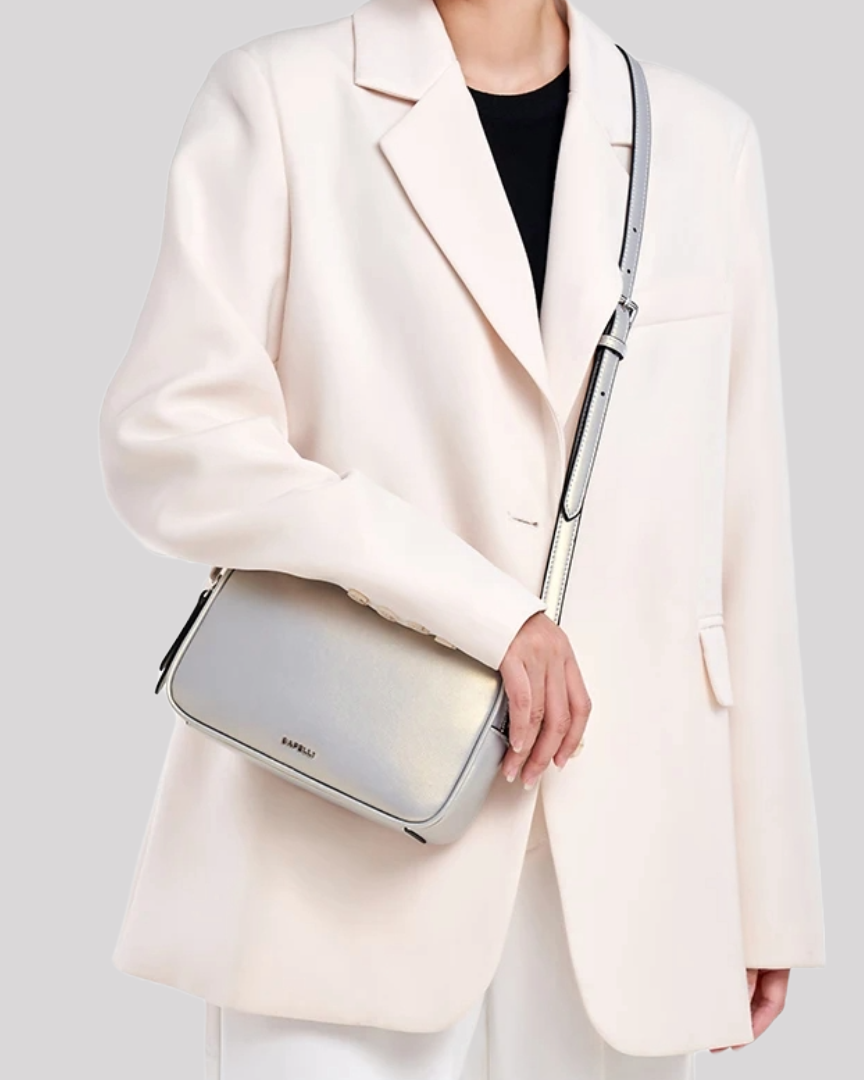 Silver leather crossbody bag by Bafelli worn by model with white blazer, showing front view and adjustable strap